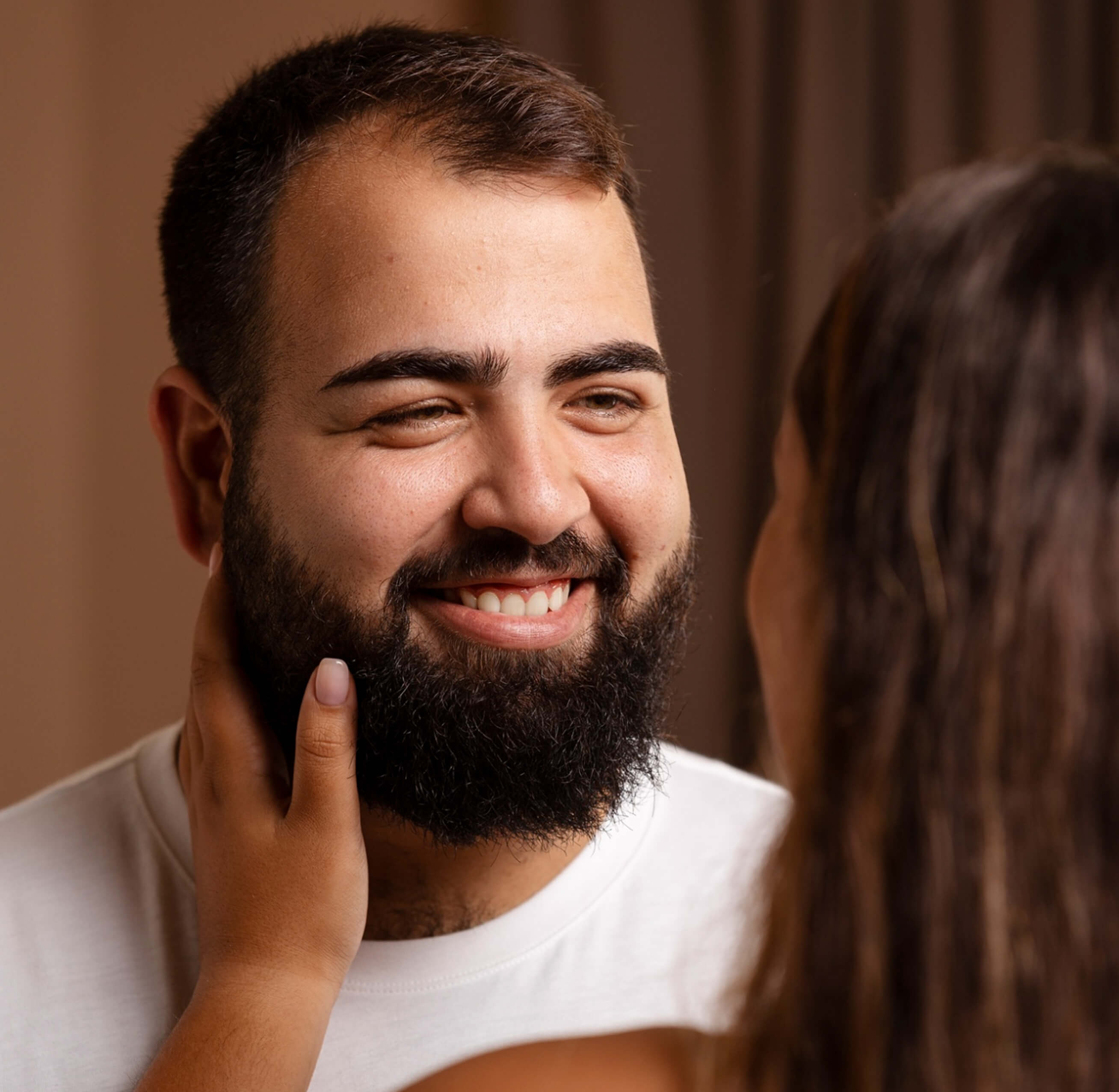 Man smiling with a beard, woman touching his face.