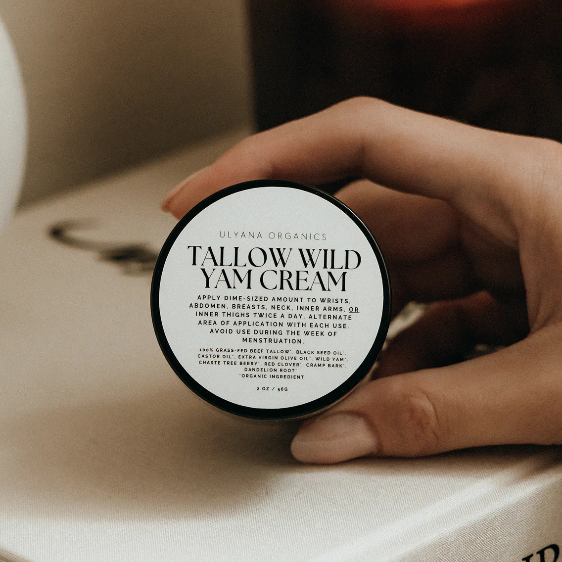 Hand holding a jar of Tallow Wild Yam Cream on a table.
