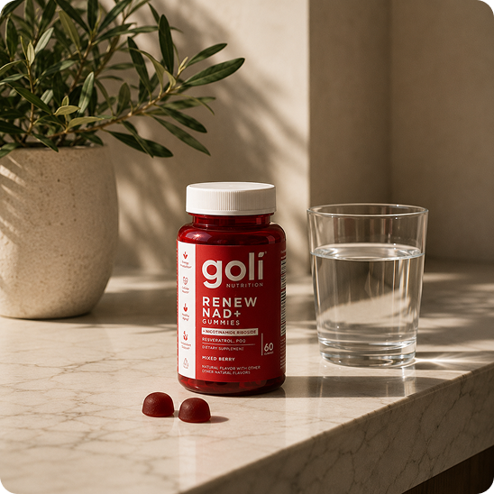 A red bottle of Goli Renew NAD+ Gummies sits on a marble countertop next to a glass of water.