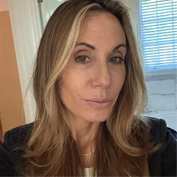 A headshot of a woman with long, light brown hair with blonde highlights, looking toward the camera.