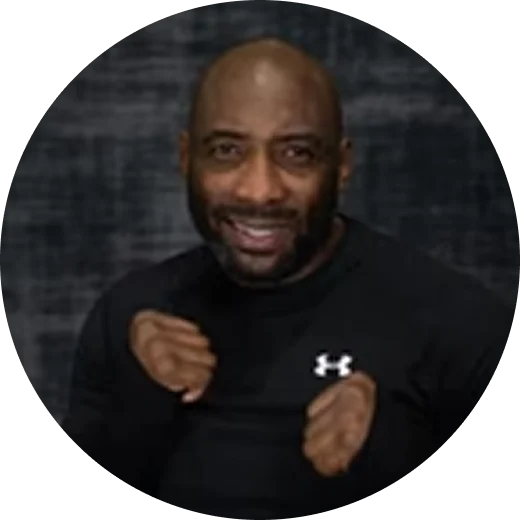 A smiling bald man with a beard, wearing a black shirt and holding his fists up.