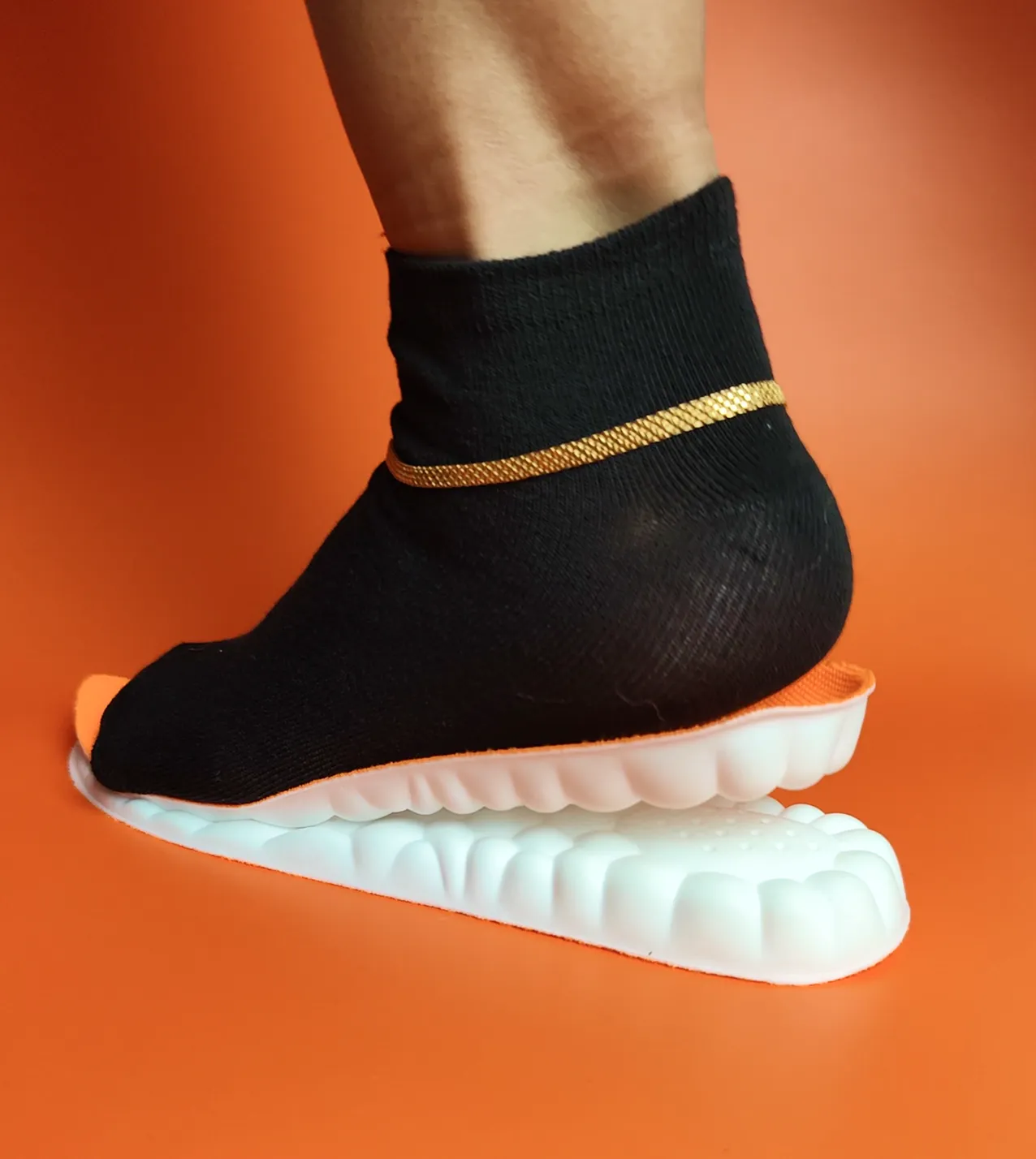Foot in a black sock on a textured white sole against an orange background.
