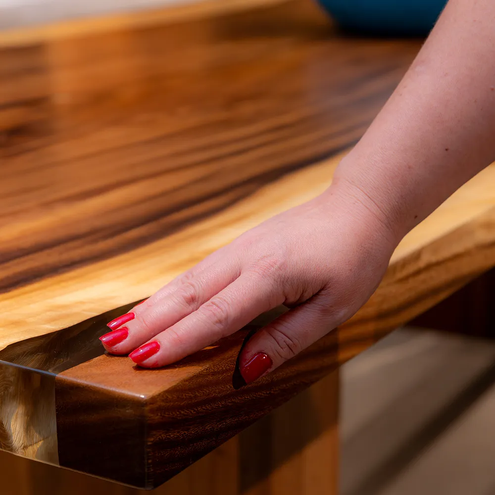 A close-up of a hand with red nail polish touching the glossy surface of a wooden table.