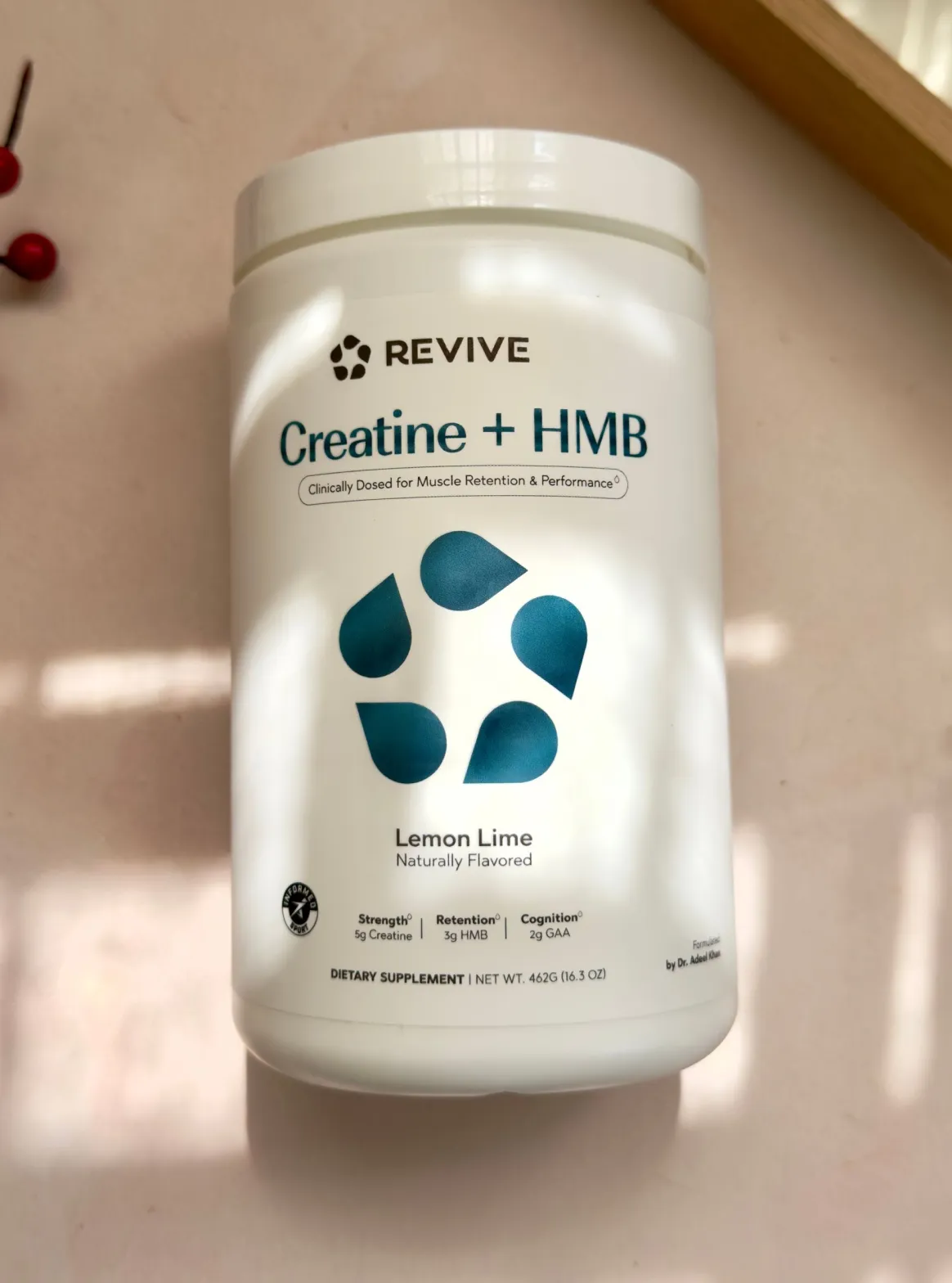 A muscular person scoops white powder from a container of Revive Creatine + HMB dietary supplement.