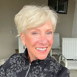 A smiling woman with short platinum blonde hair, wearing a black and white patterned jacket.