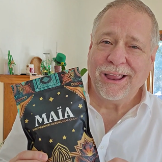 Man holding a bag of MAIA ceremonial cacao, smiling indoors.
