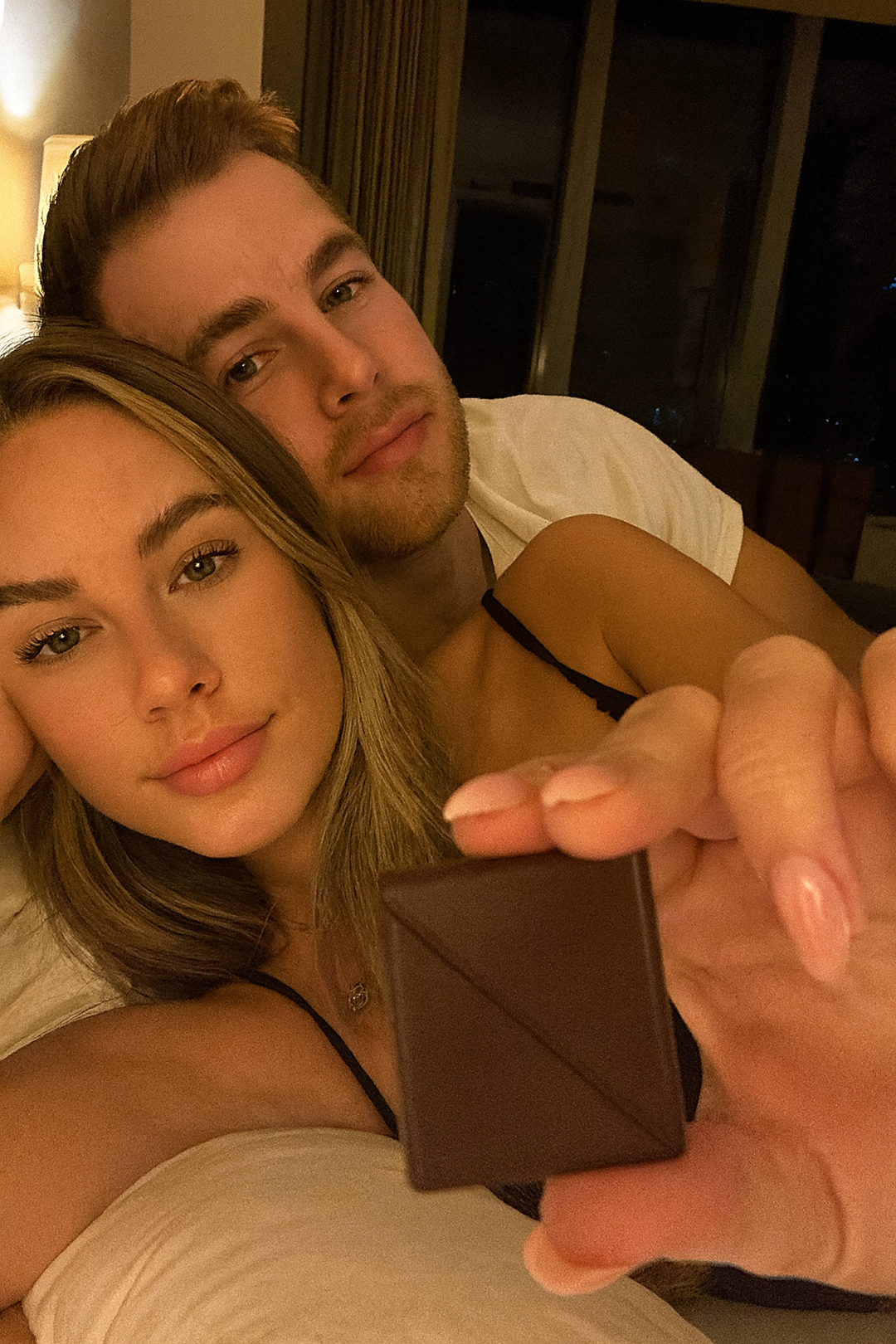 A couple relaxing in bed, holding a piece of chocolate.