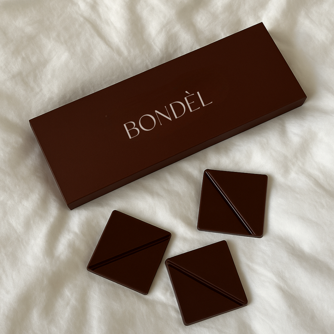 Brown box labeled 'BONDÈL' with three geometric chocolate pieces on white fabric.