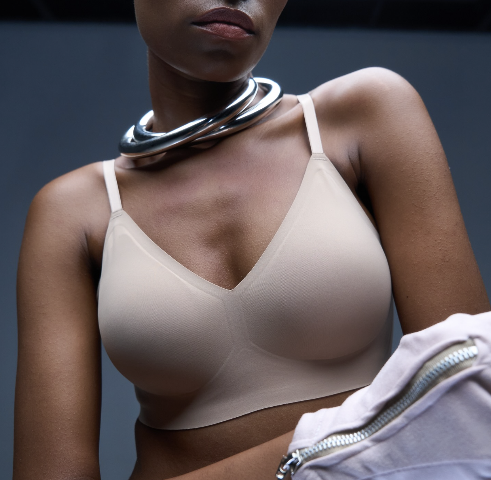 Person wearing a beige bra and silver necklace, holding a white garment.