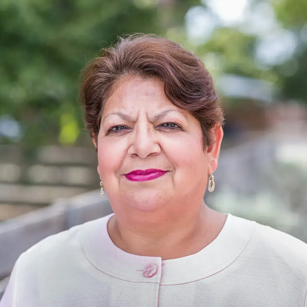Person with short brown hair, wearing light clothing and earrings, standing outdoors.