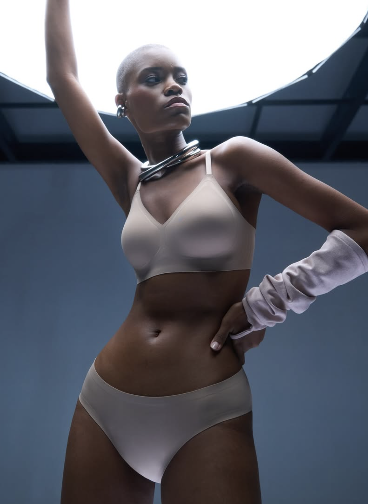 Person posing in beige underwear under a circular light.