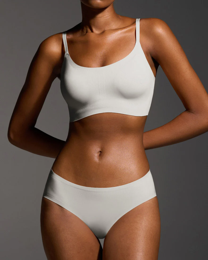 Person wearing a light-colored bra and underwear set against a gray background.