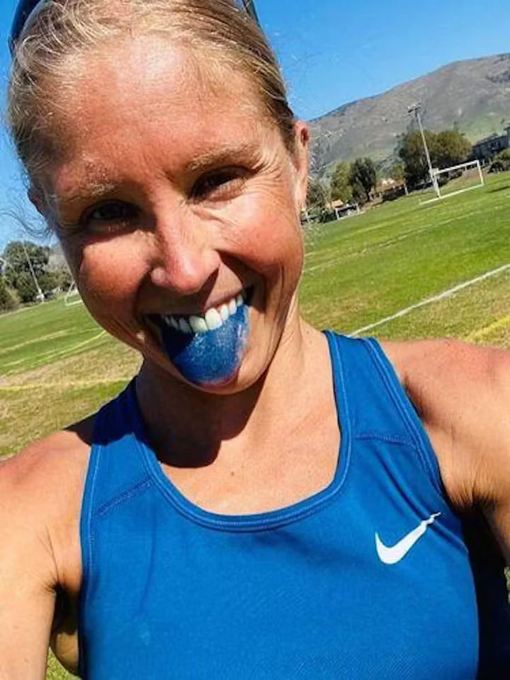 Person in blue tank top with blue tongue, smiling outdoors.