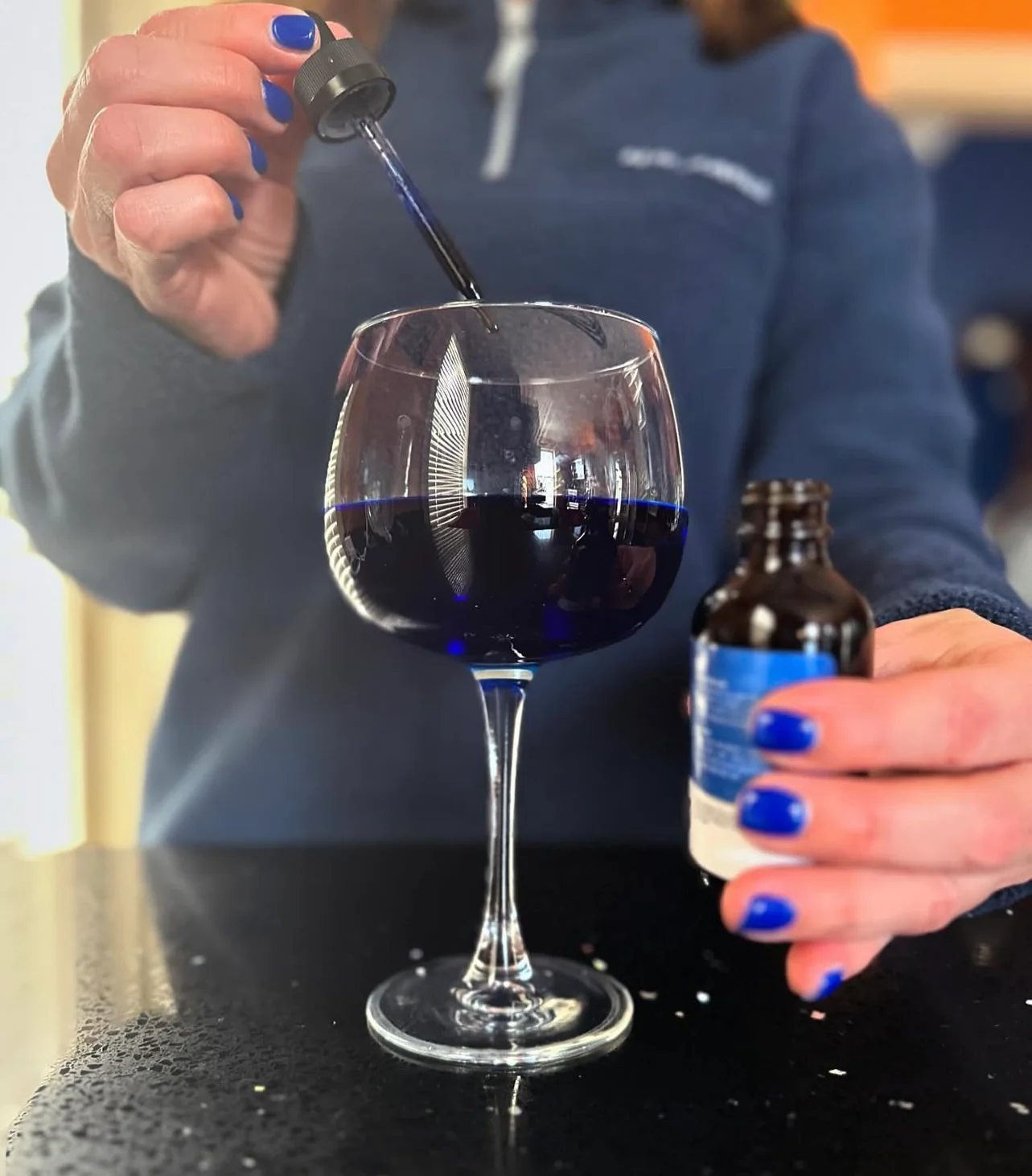 Person adding blue liquid to a wine glass with a dropper.