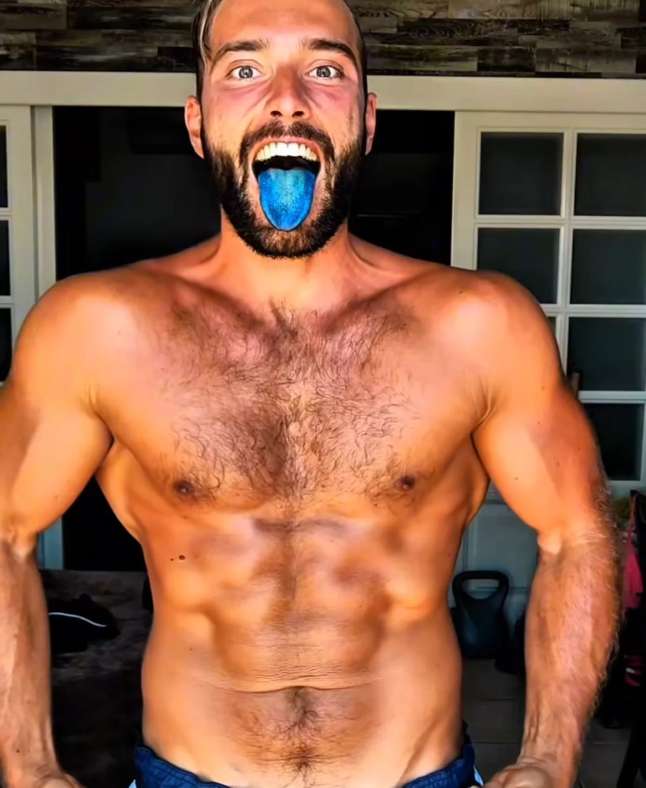 Shirtless man with a blue tongue, standing indoors.