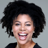 Headshot of a Black woman with natural hair smiling broadly at the camera against a grey background.