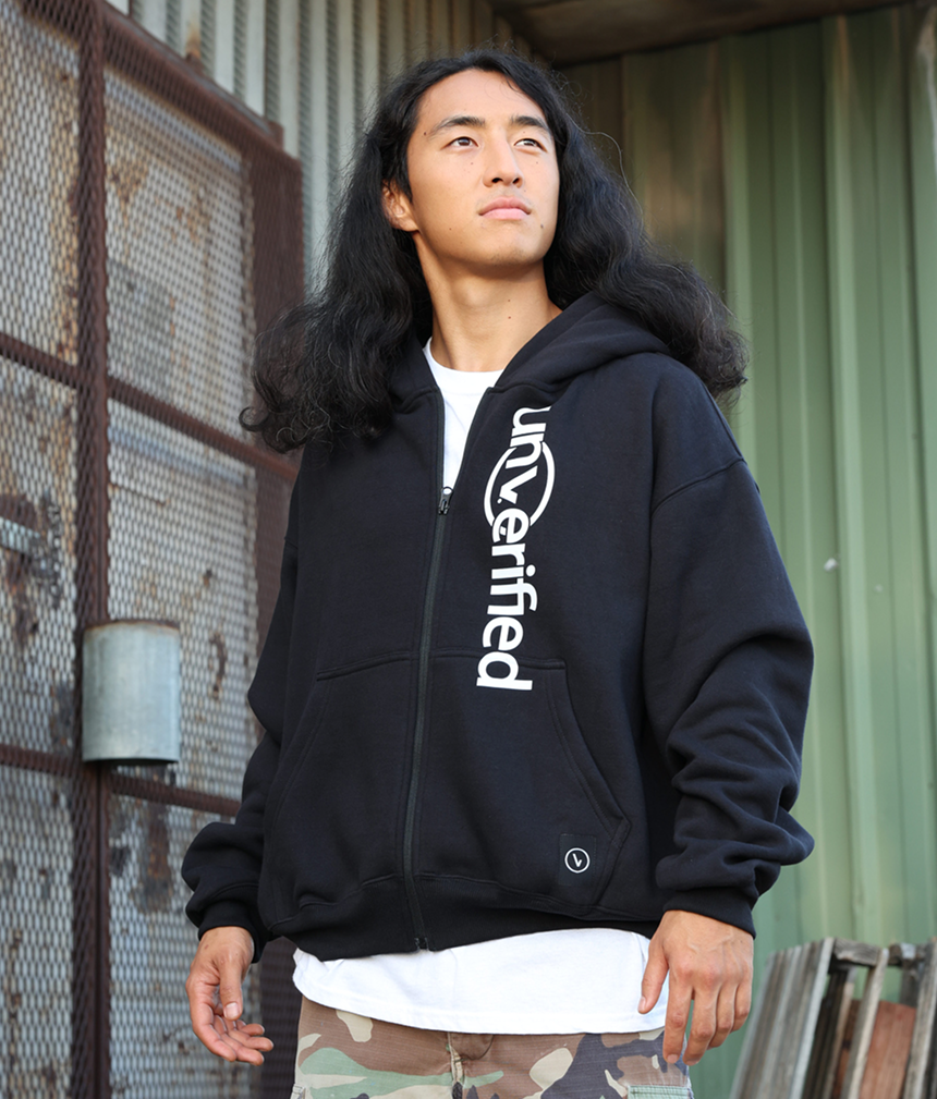 Person in a 'unverified' hoodie stands outdoors against a metal background.