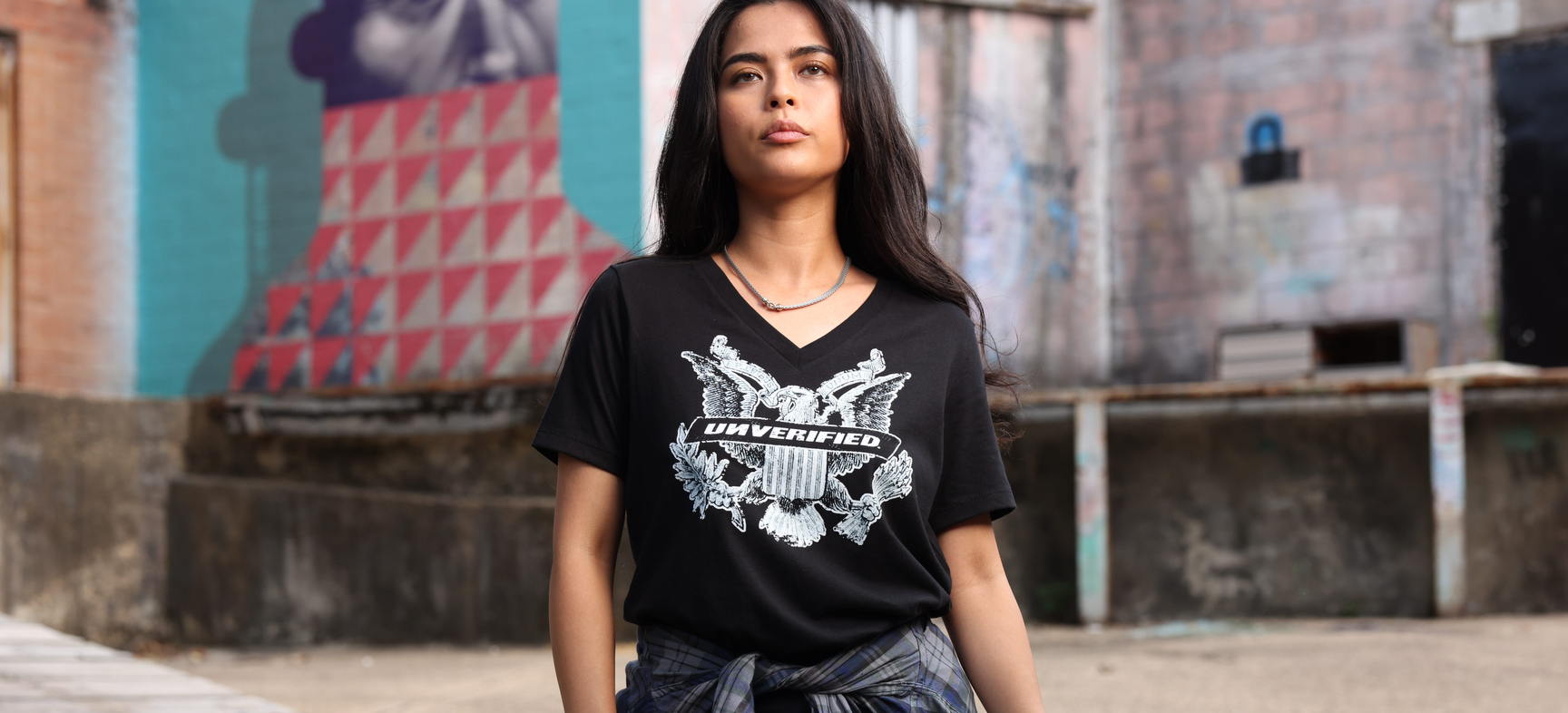 Person wearing a black 'UNVERIFIED' t-shirt standing in front of a colorful mural.