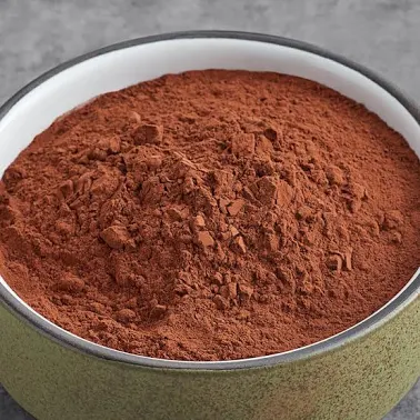 A close-up of a green bowl with a white rim, filled with a reddish-brown powder.