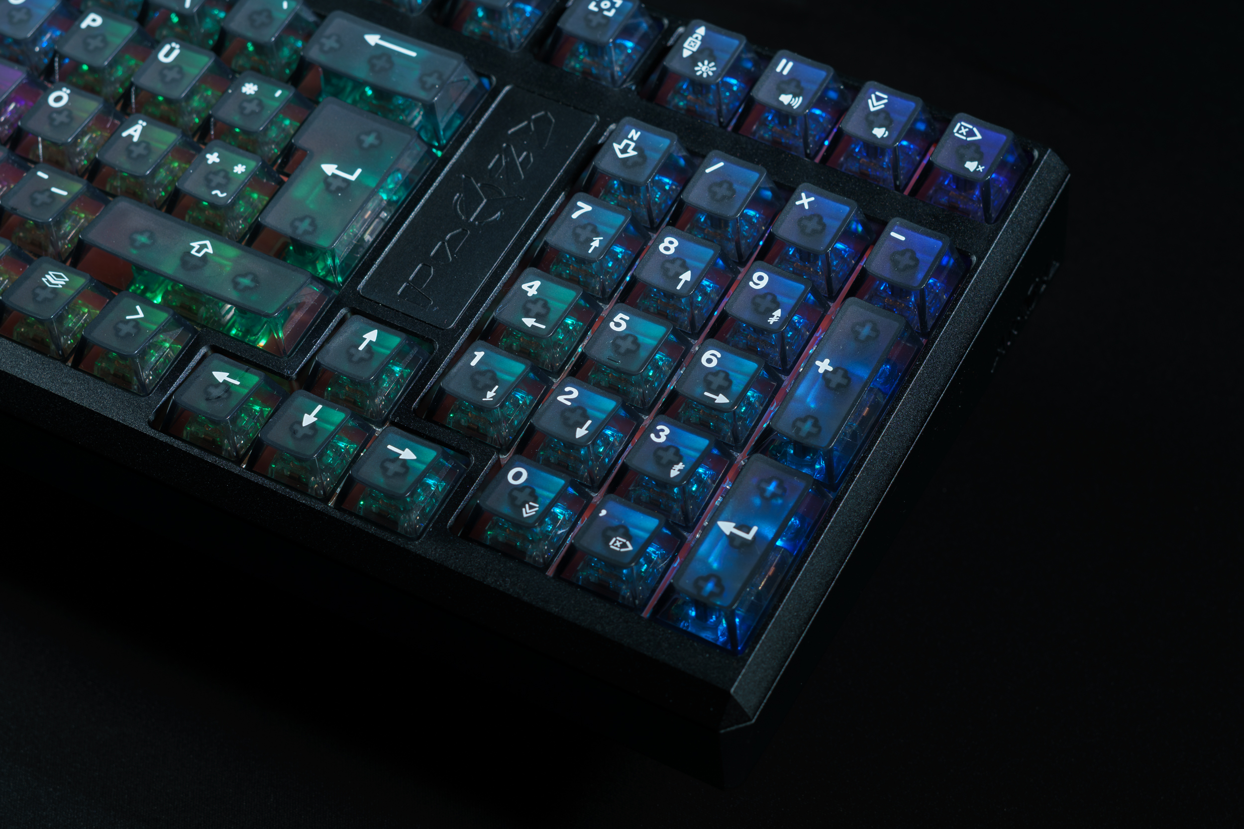 A close-up of a backlit mechanical keyboard with translucent blue and green keycaps on a black background.