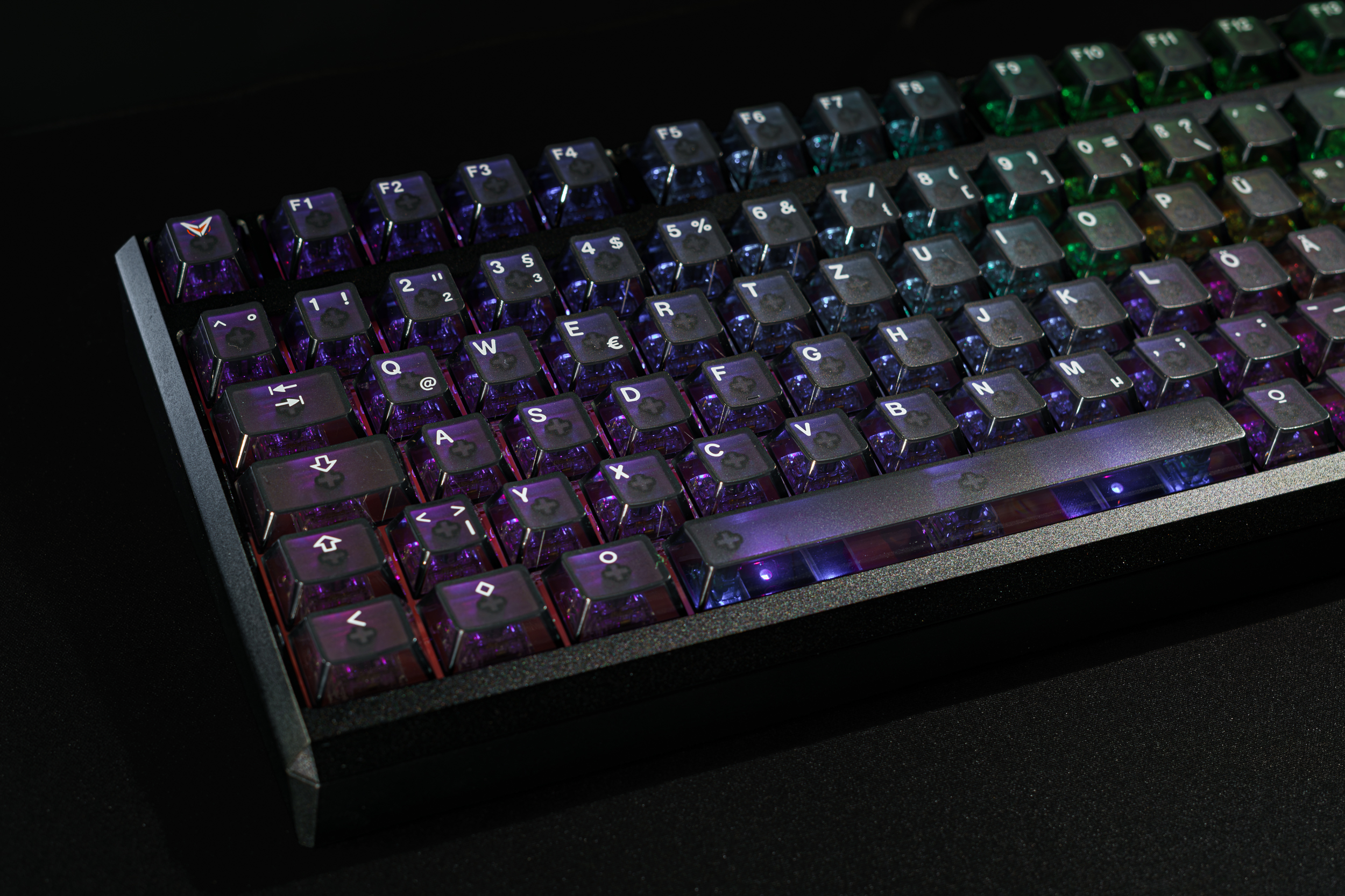 A close-up of a backlit mechanical keyboard with translucent, multicolored keycaps on a dark surface.
