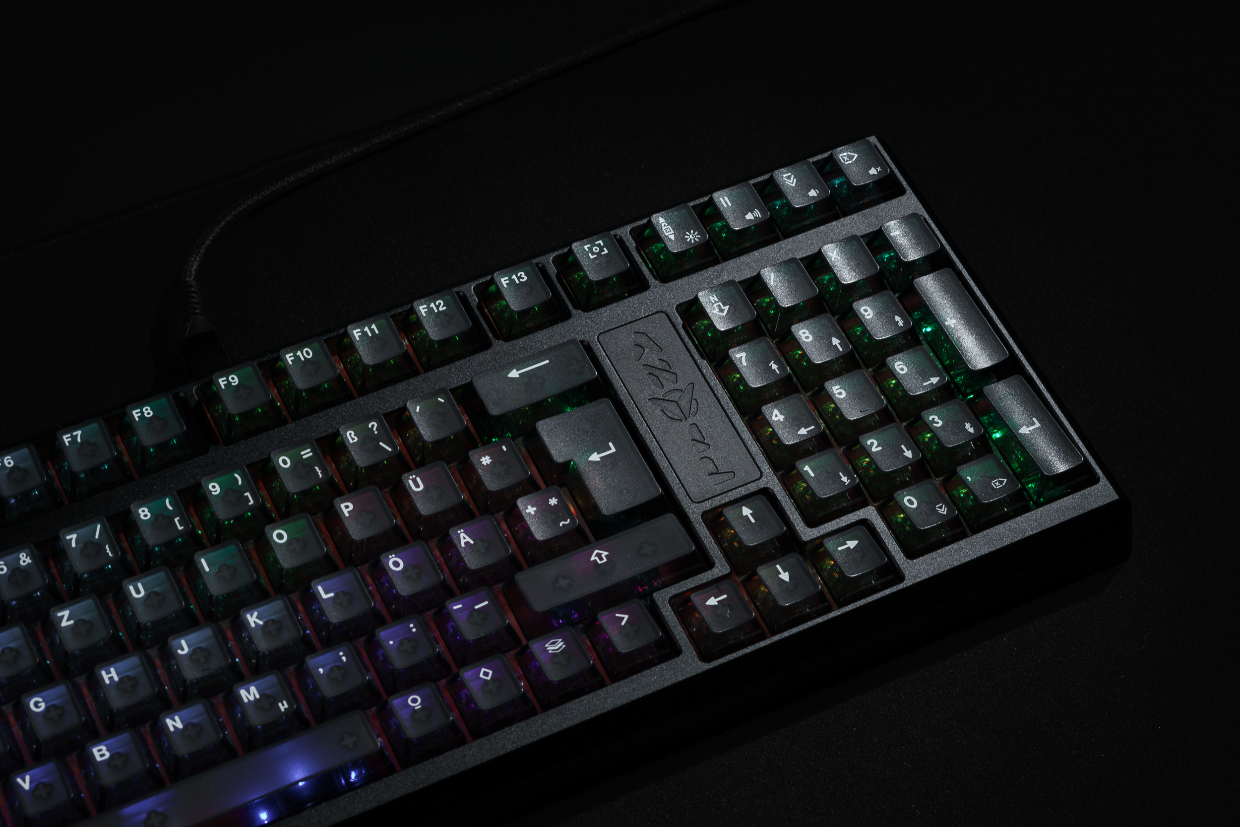 A close-up, angled view of a black keyboard with multi-colored backlighting against a dark background.