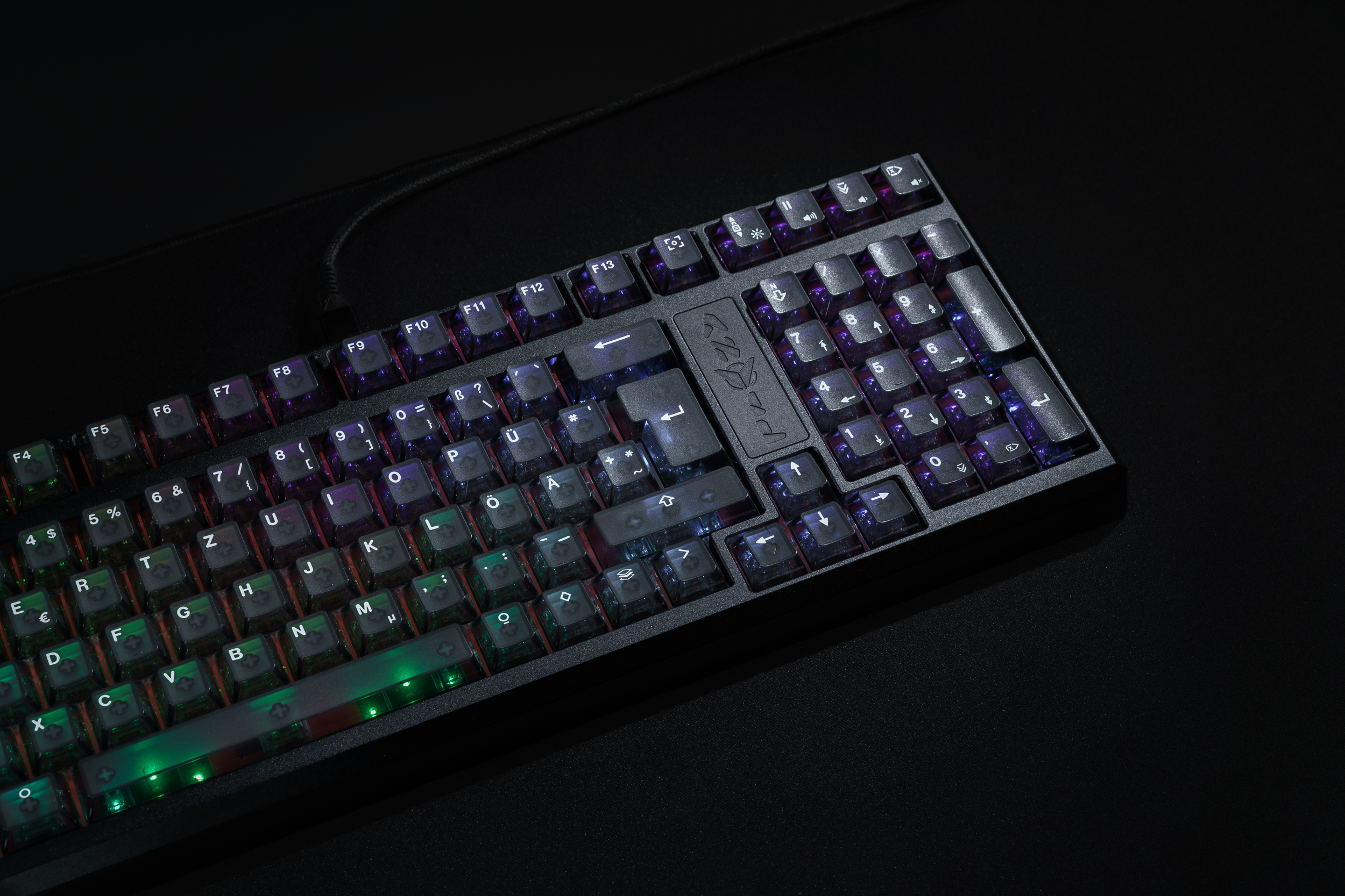 A close-up, angled view of a black mechanical keyboard with multi-colored backlighting on a dark surface.