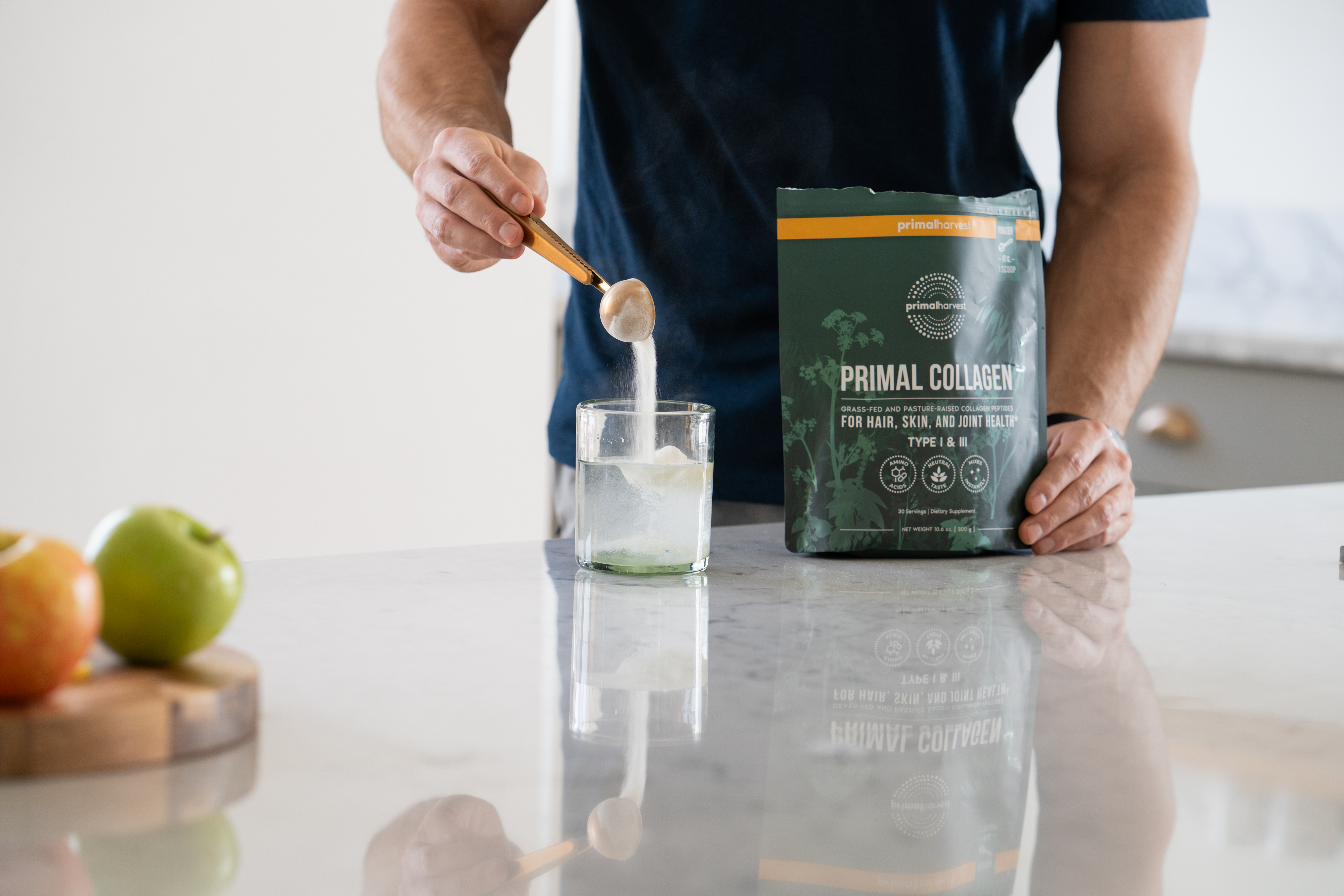 Person adding collagen powder to a glass on a kitchen counter.