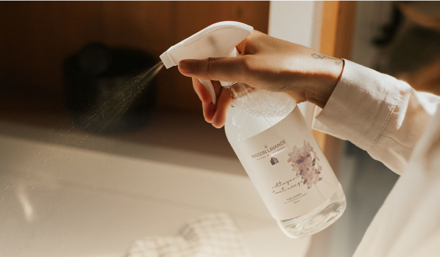 Hand spraying bottle of cleaning solution with lavender label.
