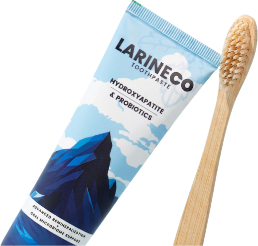 A tube of Larineco brand toothpaste is shown next to a wooden toothbrush against a white background.