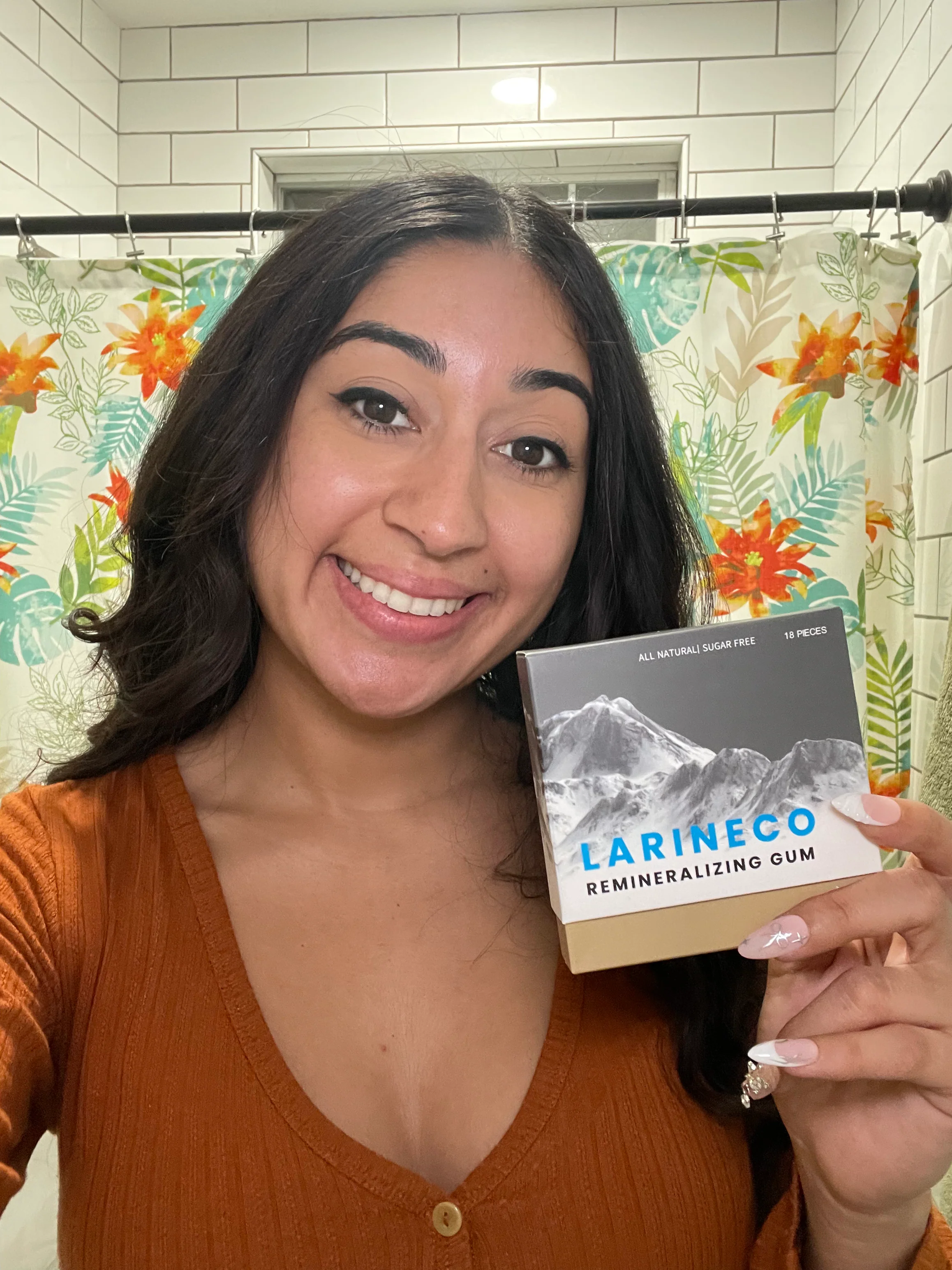 Person smiling, holding a box of LARINECO remineralizing gum in a bathroom.