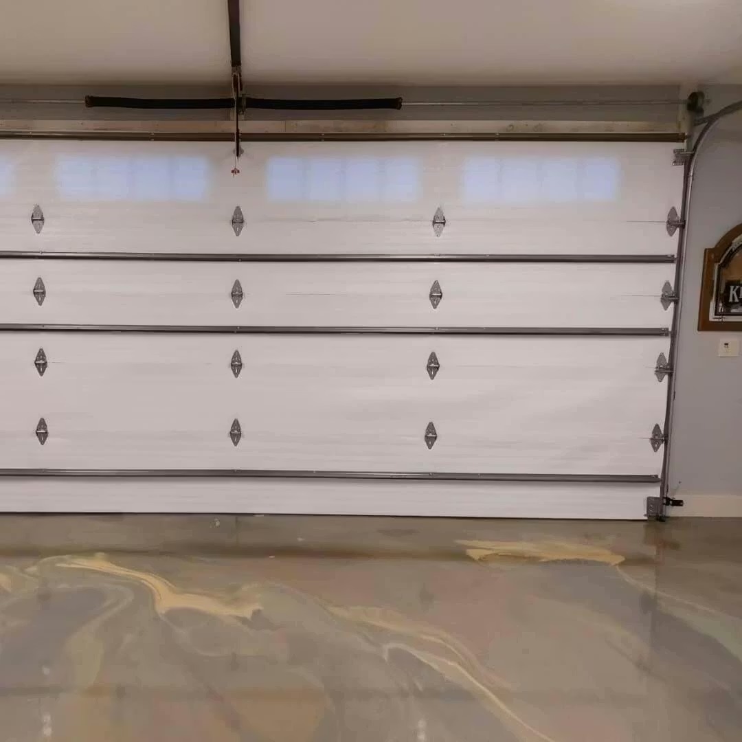 The interior of a garage with a white sectional door and a glossy, swirled epoxy floor.