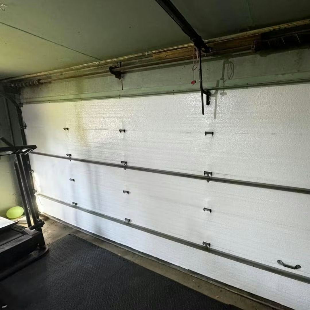 The inside of a white, insulated, sectional garage door next to a treadmill.