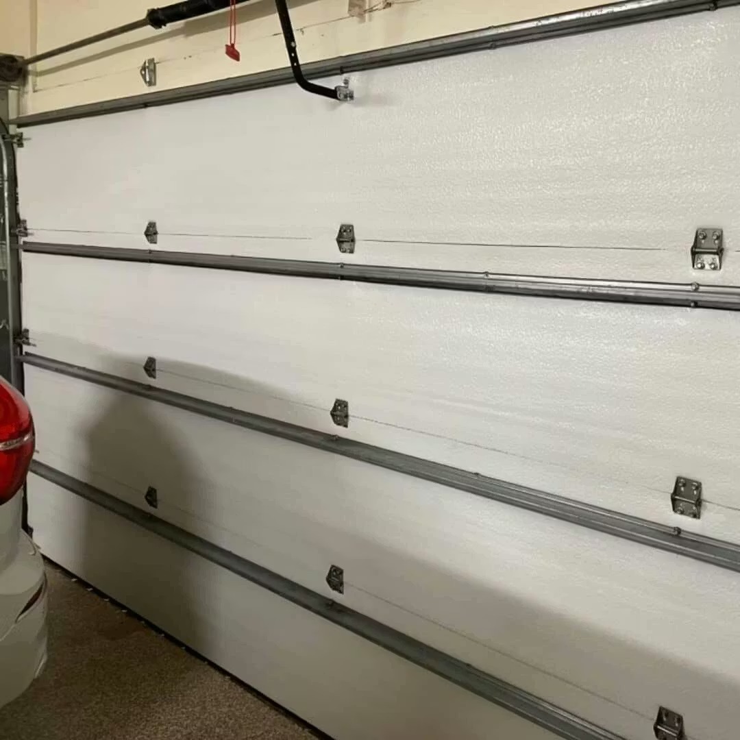 The inside of a white, four-panel sectional garage door with its hardware and a car parked nearby.