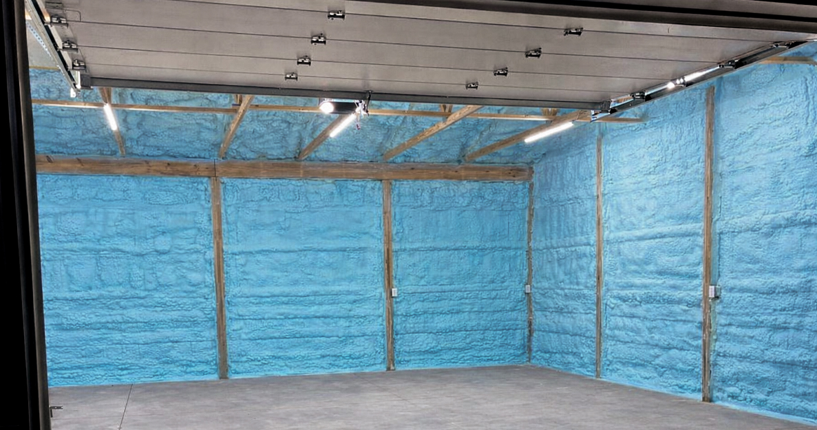 The interior of a large garage with light blue spray foam insulation on the walls between wooden beams.