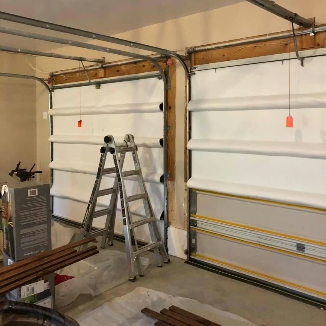 A stepladder stands in front of two garage doors being fitted with white insulation panels.