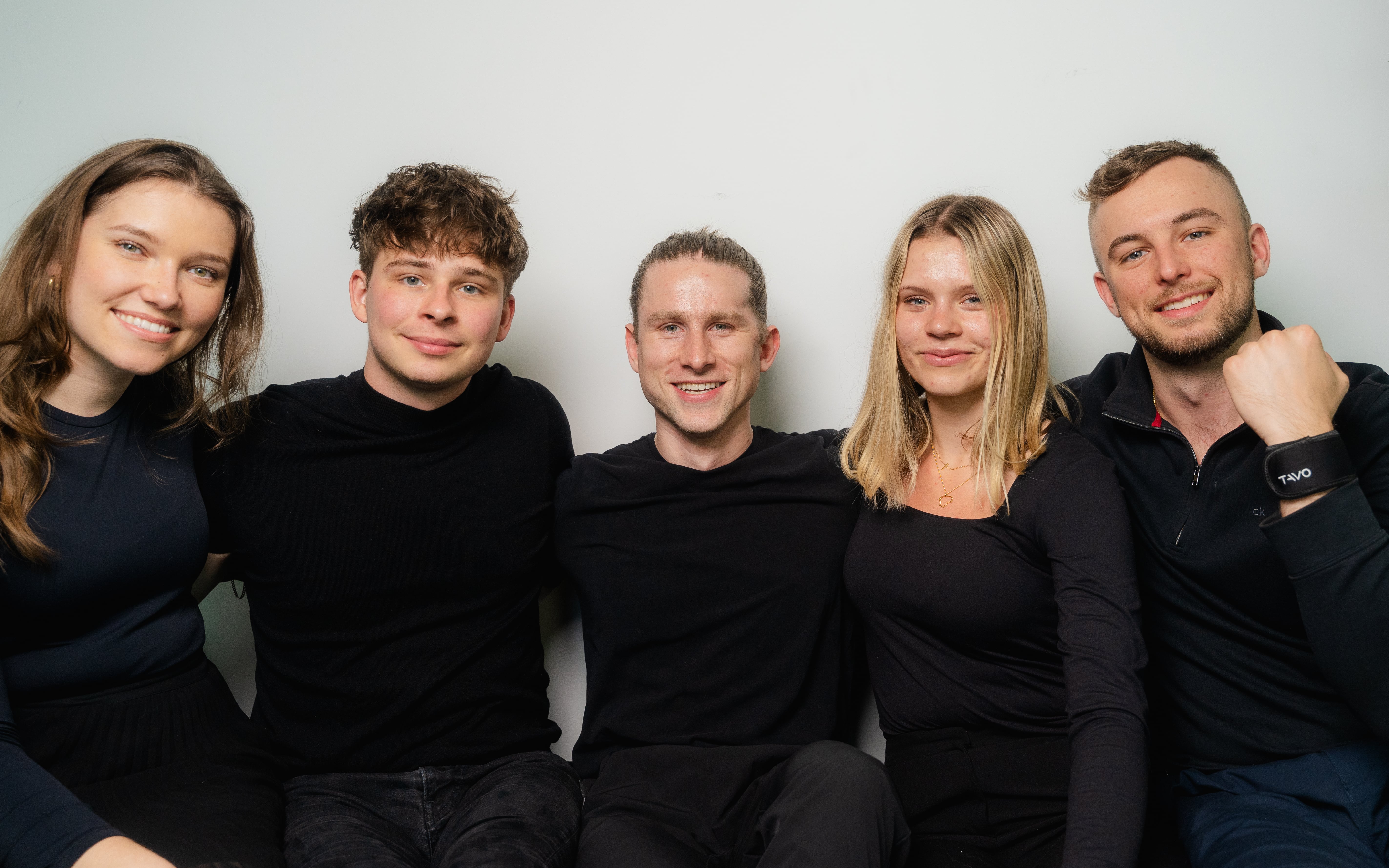 A group of five people smiling, seated close together.