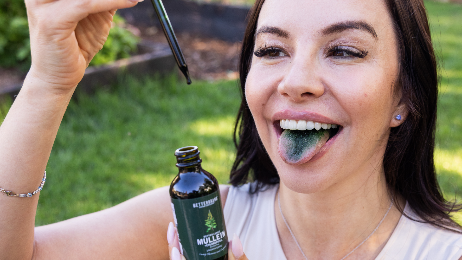 Person with blue tongue holding dropper and bottle outdoors.