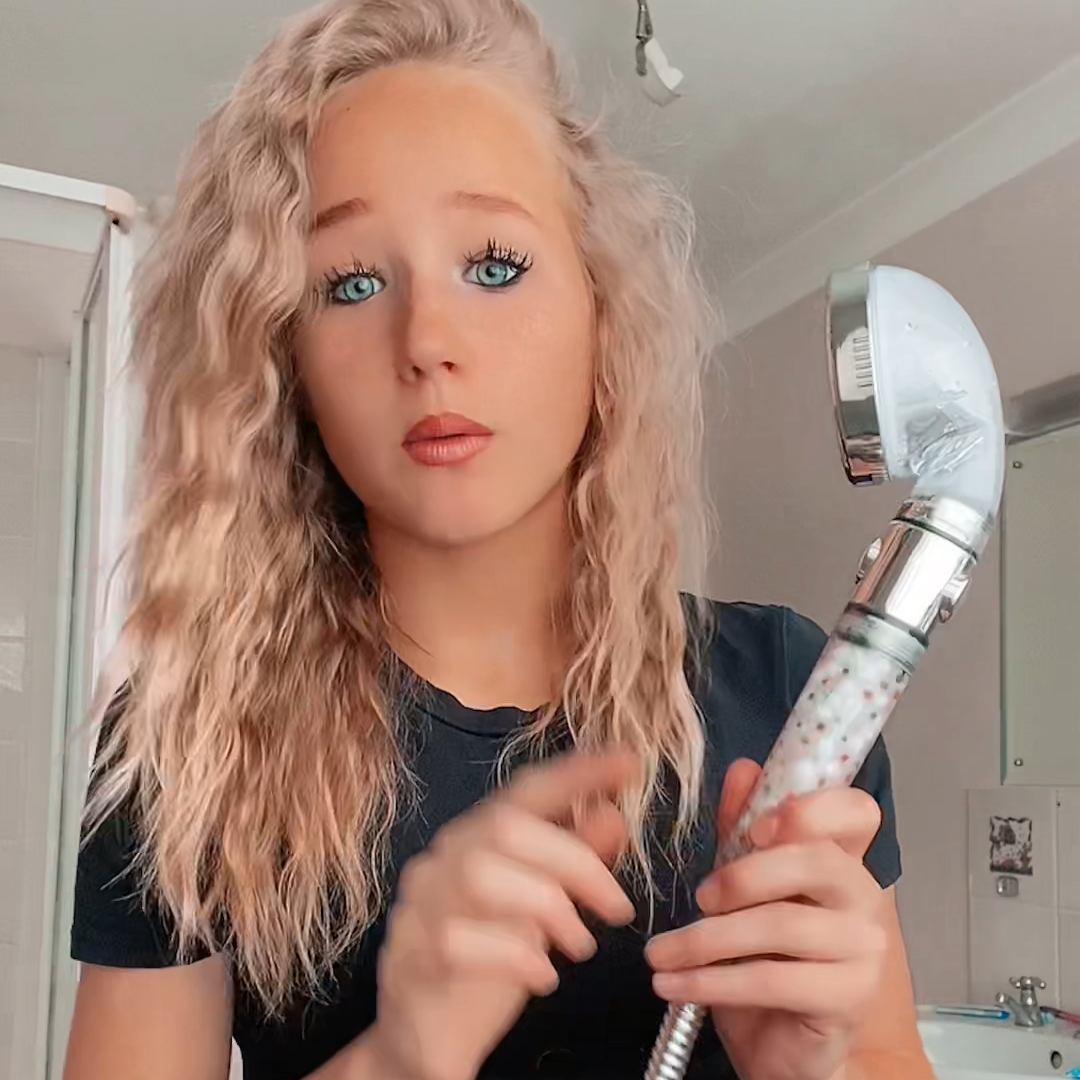 Person holding a showerhead in a bathroom setting.
