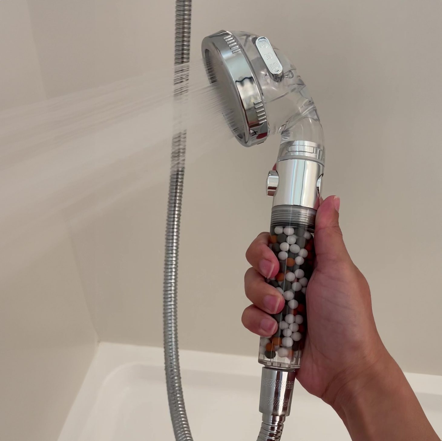 Hand holding a showerhead with mineral beads, water spraying.