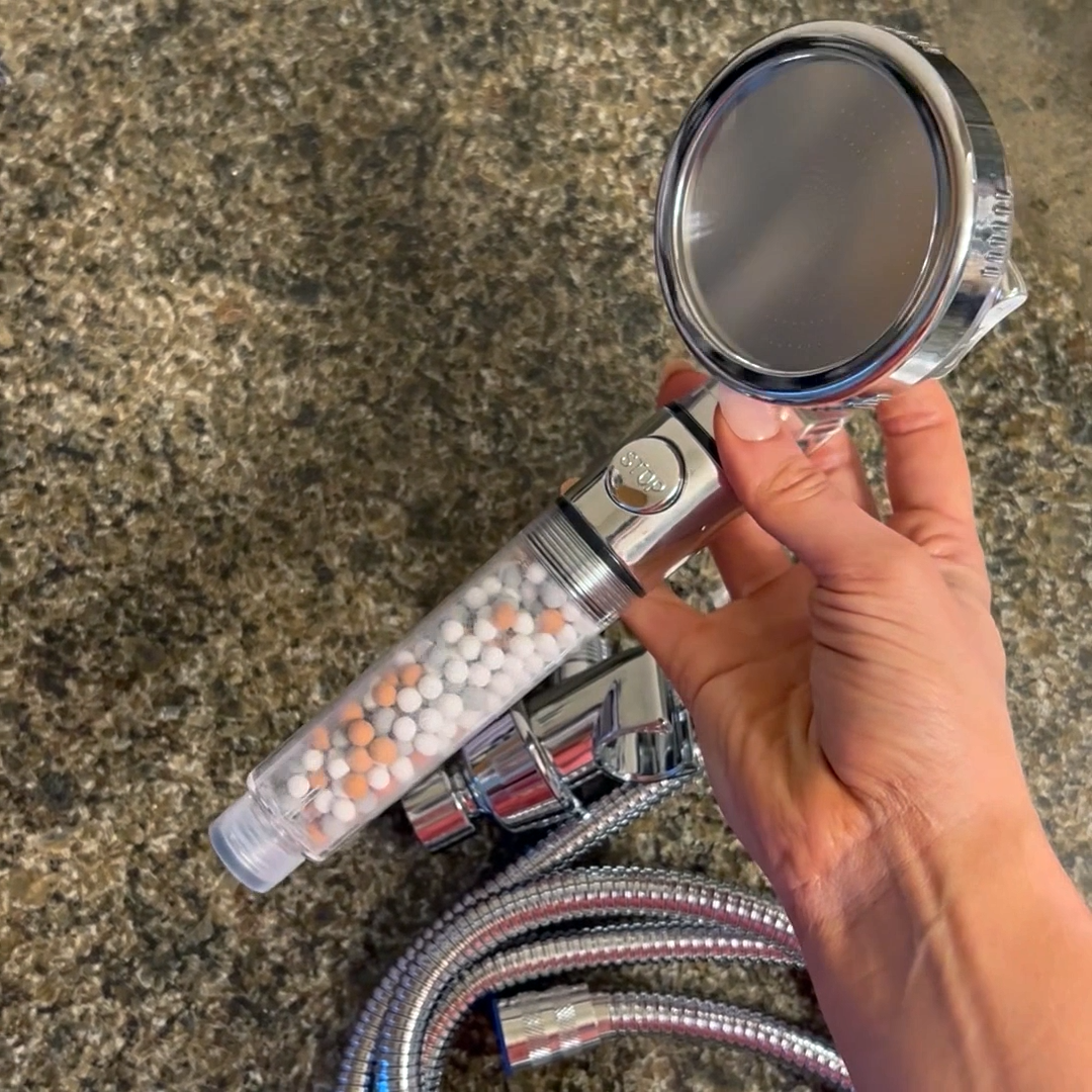 Hand holding a shower head with mineral beads and a metal hose.