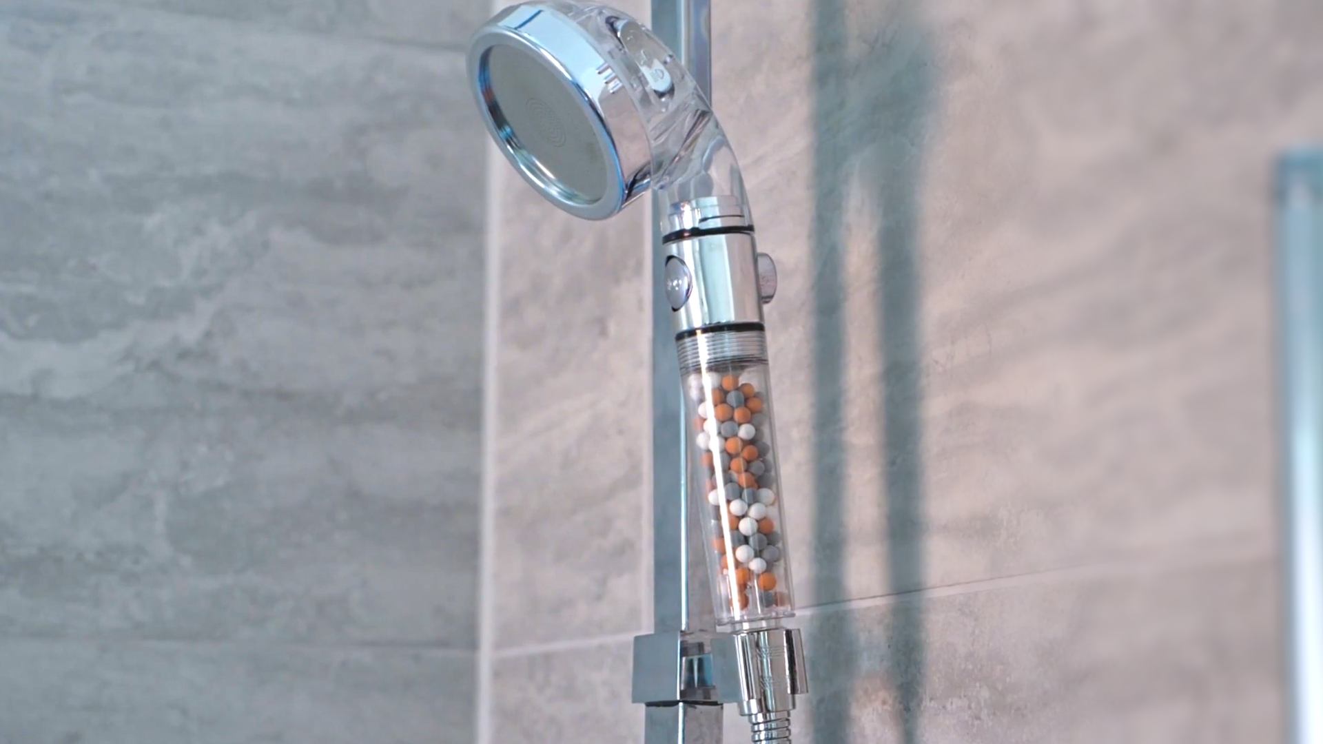Showerhead with mineral filter beads attached to a tiled bathroom wall.