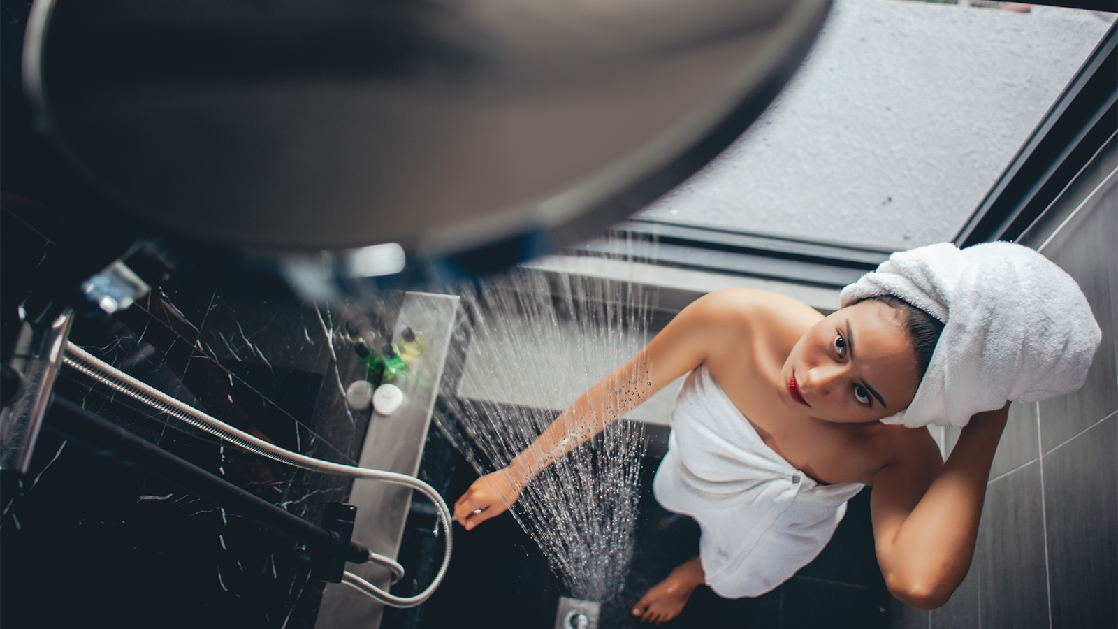 Person in a shower with a towel wrapped around their body and head.