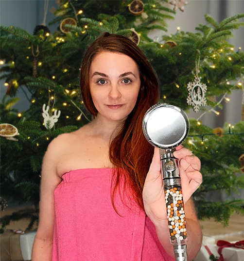 Person in a pink towel holding a showerhead in front of a decorated Christmas tree.