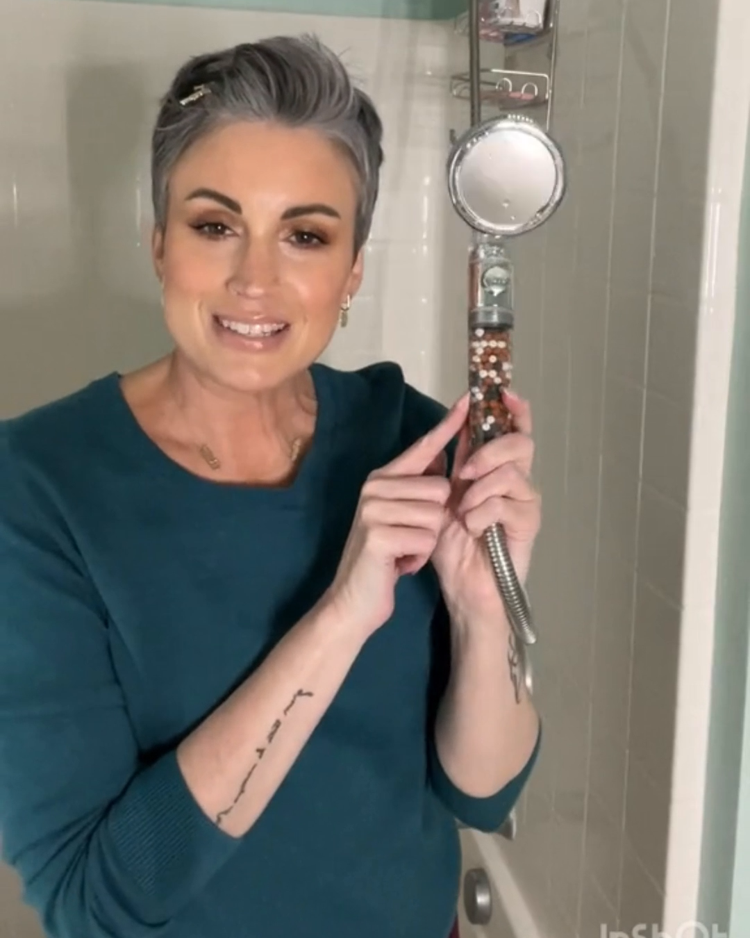 Person holding a showerhead with mineral beads in a bathroom.