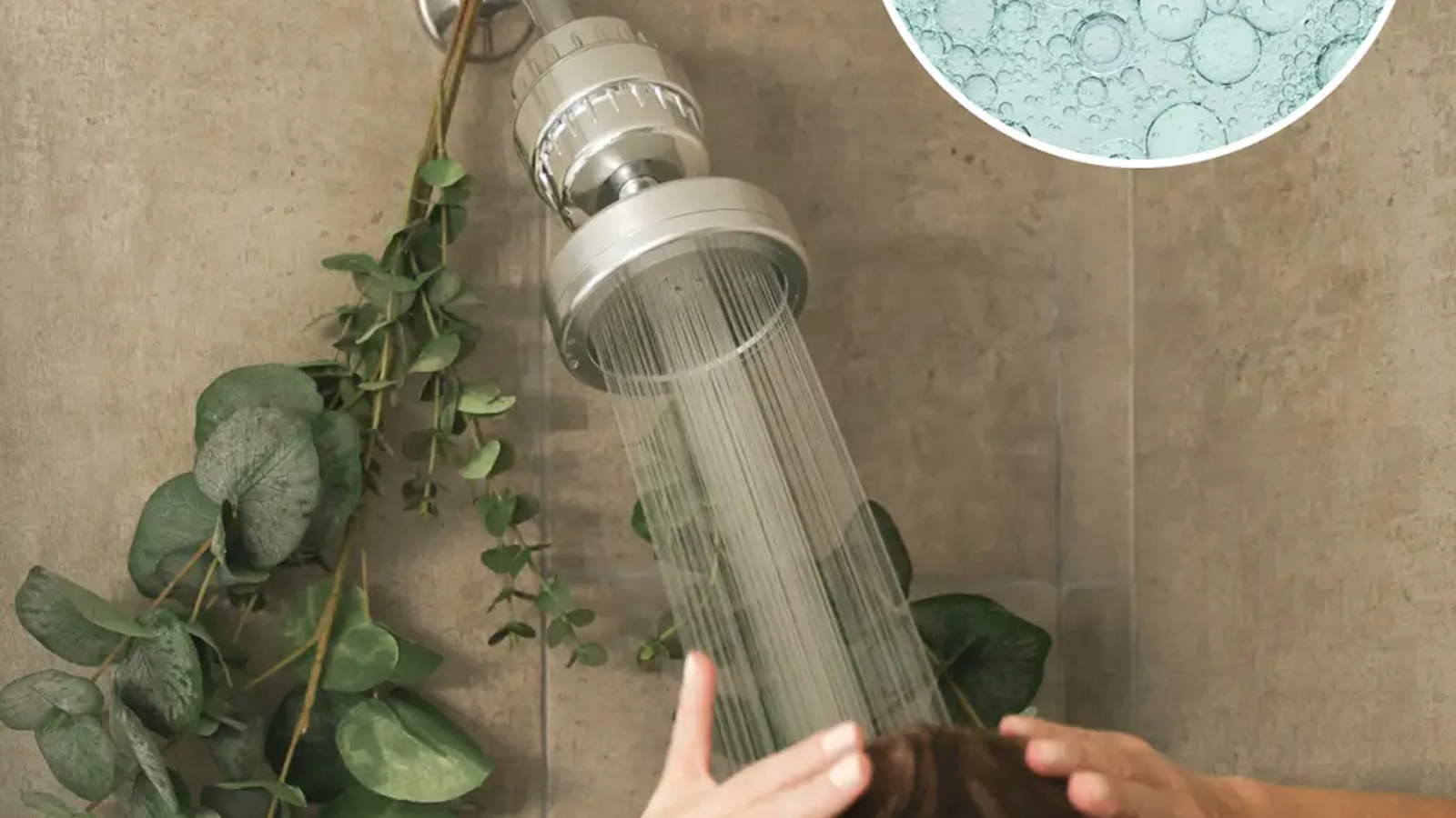 Showerhead with water flowing, eucalyptus leaves hanging nearby.