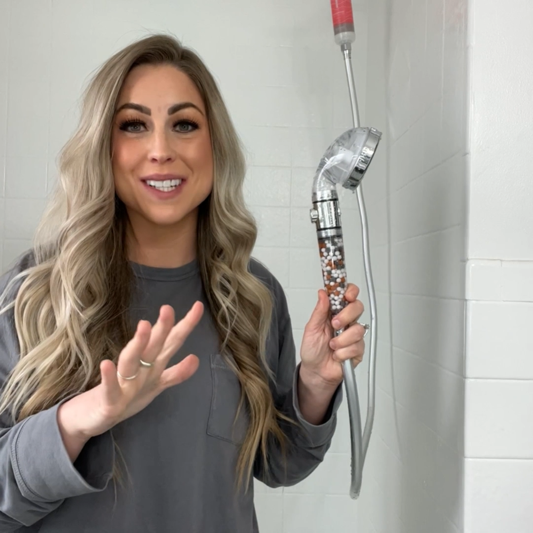 Person holding a showerhead with mineral beads in a bathroom.
