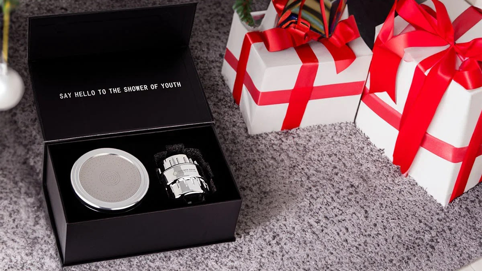 Open black box with shower filter, next to wrapped gifts with red ribbons.