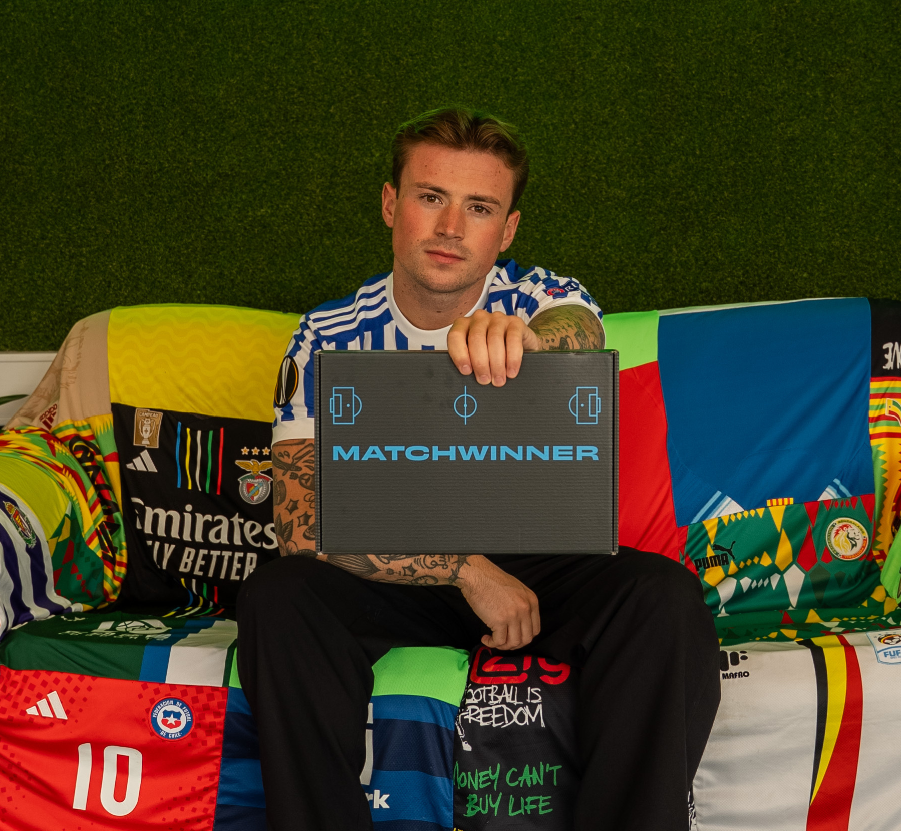 A man in a striped jersey holds a 'MATCHWINNER' box while sitting on a couch made of jerseys.