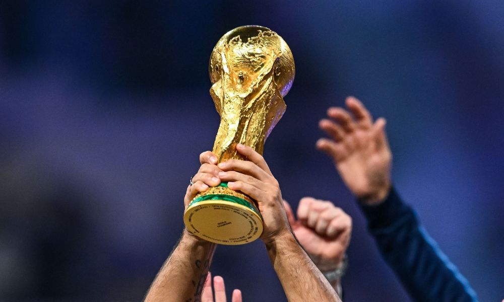 A pair of hands holds the golden FIFA World Cup trophy high in the air in celebration.